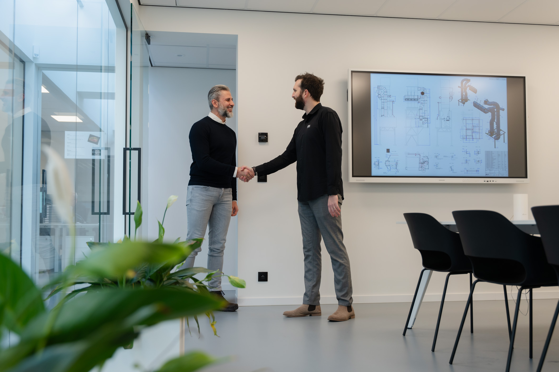 Een medewerker ontvangt een klant in een meeting room met een scherm waarop een ontwerp te zien is.